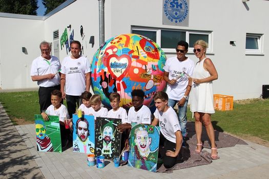 Nachwuchskicker von Anpfiff ins Leben e.V. und SGK mit ihren Kunstwerken vor dem gestalteten überlebensgroßen Fußball.